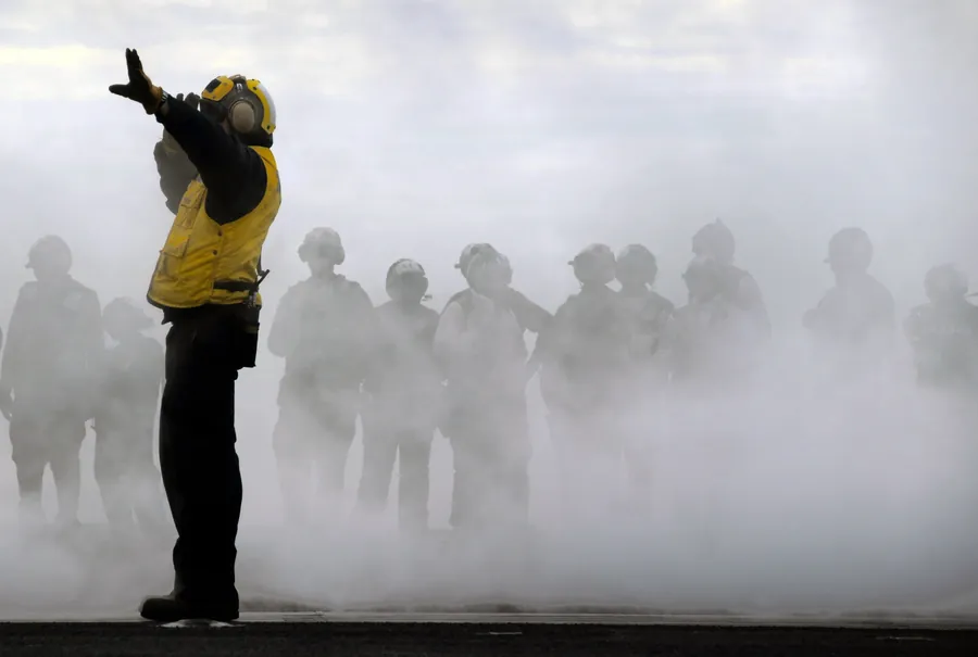 A figure in a yellow jersey directing a crowd through fog